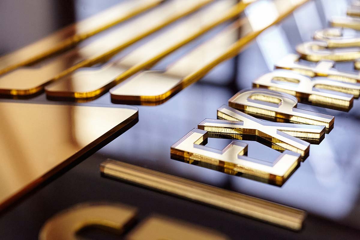 Detalle de letrero de acrilico negro y espejo oro gold