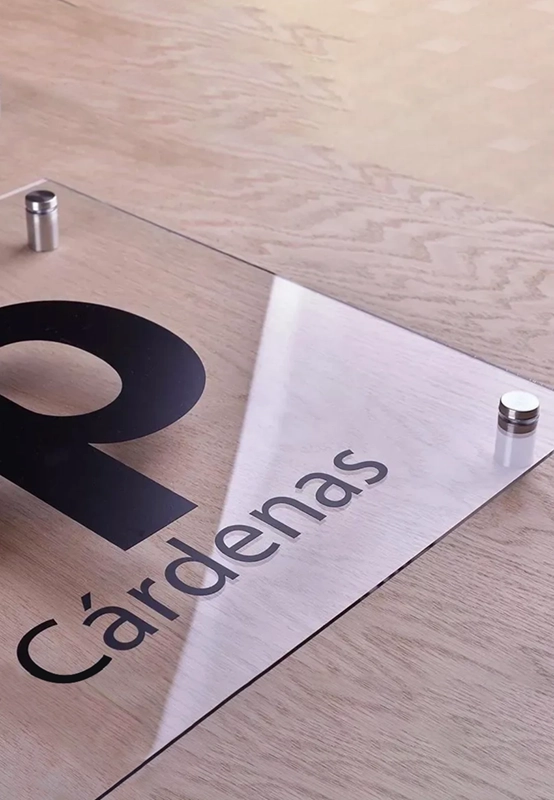 Letrero personalizado de acrílico cristal con rotulación en vinil y chapetones de acero inoxidable para colocación en muro